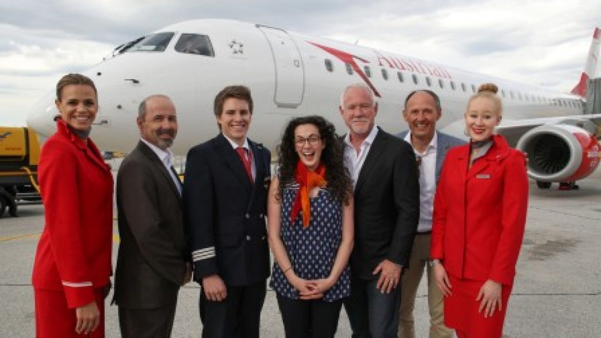 Sieben Personen posieren und lächeln vor einem Flugzeug der Austrian Airlines auf einer Flughafenpiste.