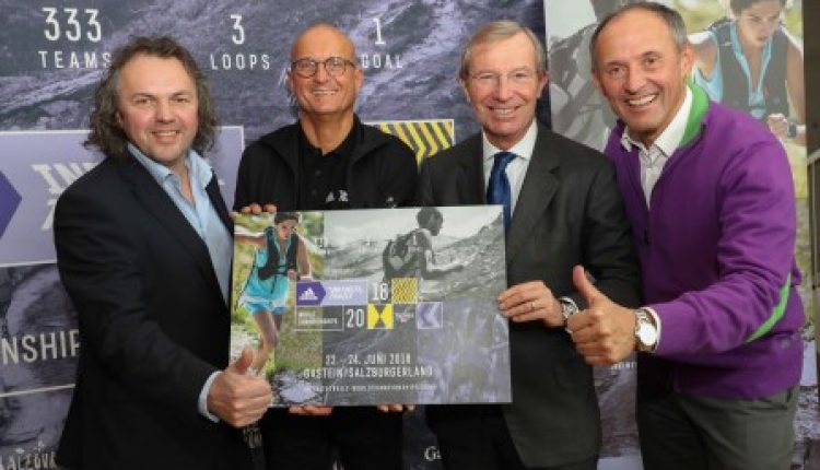 Vier Männer in Anzügen lächeln und halten ein Plakat mit einer Bergkulisse und einer Daumen-hoch-Geste.