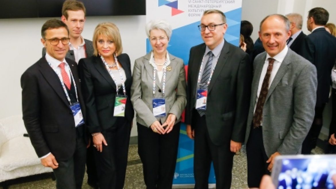 Sechs Personen in Geschäftskleidung posieren und lächeln für ein Gruppenfoto bei einer Konferenzveranstaltung.