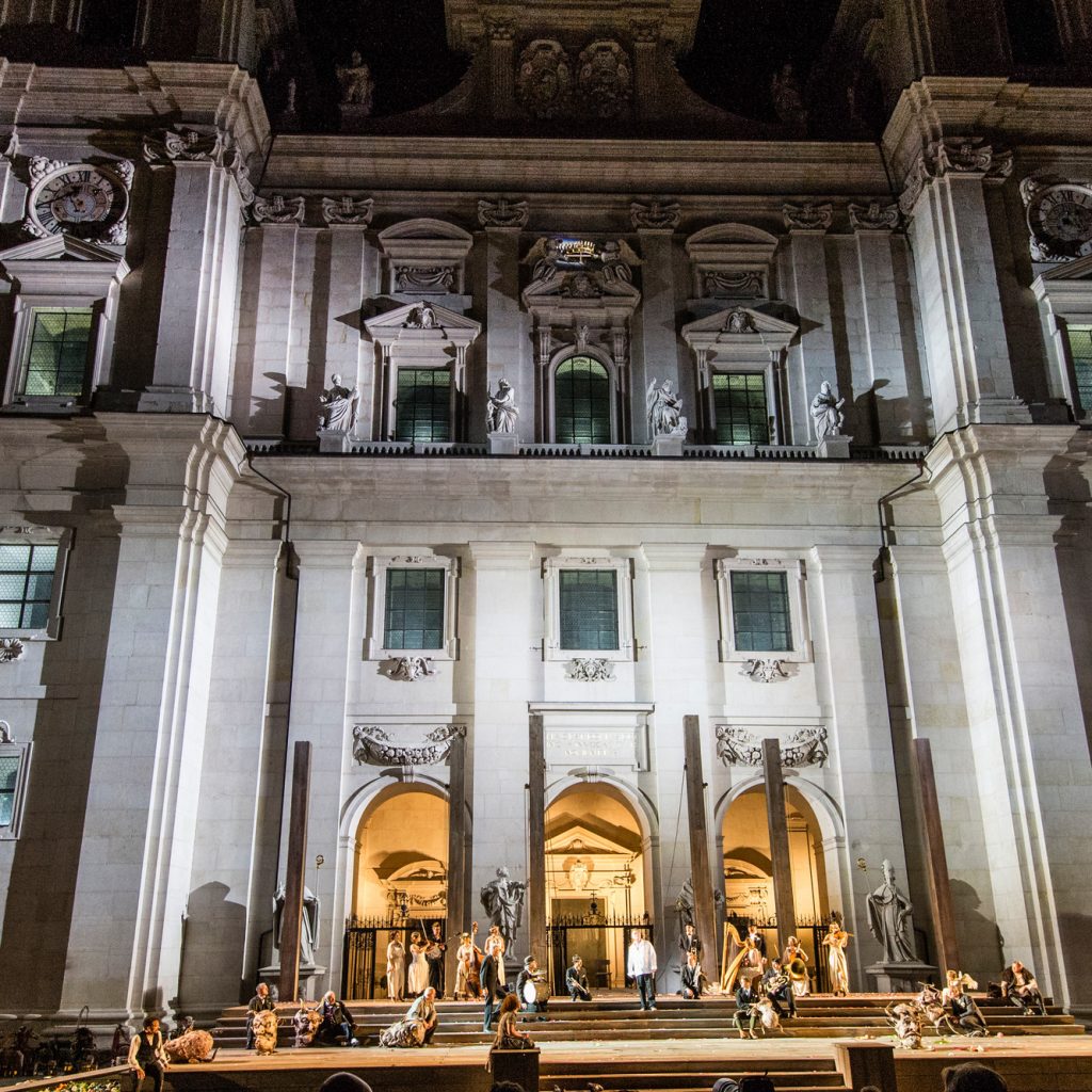Eine nächtliche Freiluftaufführung findet vor einem großen, beleuchteten historischen Gebäude statt.