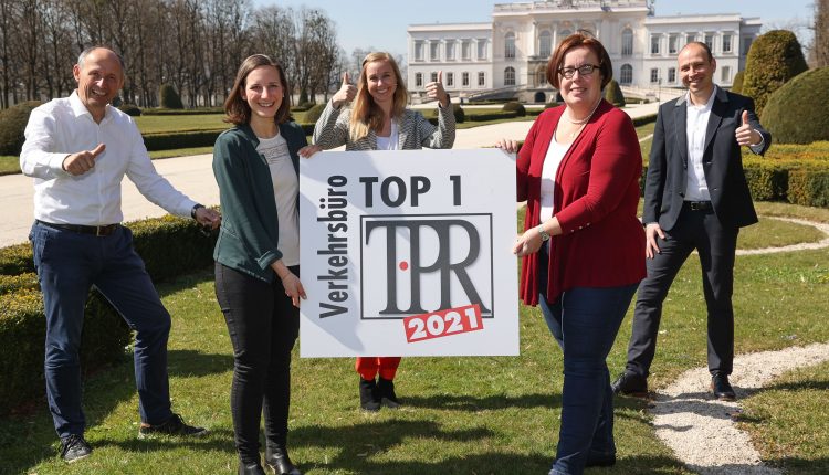 Fünf lächelnde Menschen im Freien, die ein Schild mit der Aufschrift TOP 1 Verkehrsbüro TPR 2021 halten und Daumen hoch zeigen.