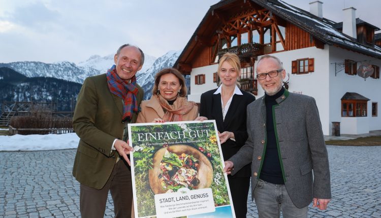 Vier lächelnde Erwachsene stehen vor einem Chalet und halten ein großes Einfach Gut-Plakat mit Lebensmittelbildern.