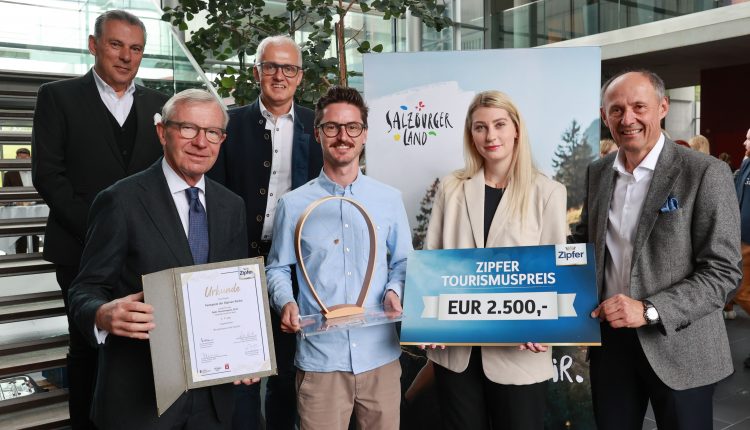Sechs Personen posieren mit einer Urkunde, einer Trophäe und einem großen Scheck über 2 500 € für den Tourismuspreis in der Halle.