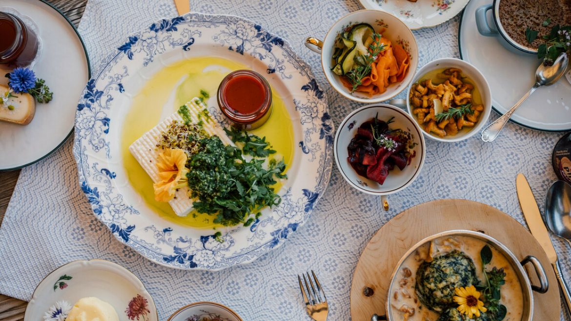 Ein Tisch mit verschiedenen bunten Gerichten, darunter Salate, Grünzeug, Soßen und Brot auf eleganten Tellern.