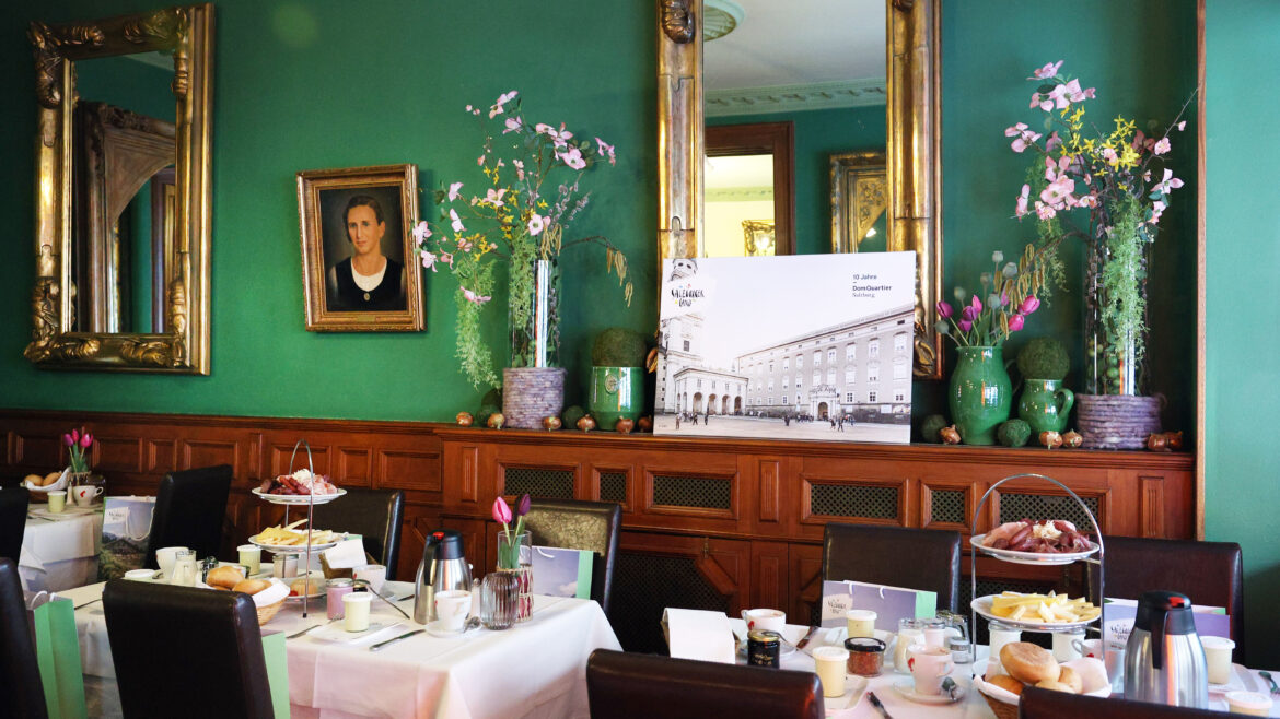 Elegantes Esszimmer mit grünen Wänden, Spiegeln, Blumen und gedeckten Tischen für das Frühstück mit verschiedenen Speisen.