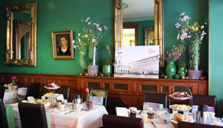 Elegantes Esszimmer mit grünen Wänden, Spiegeln, Blumen und gedeckten Tischen für das Frühstück mit verschiedenen Speisen.