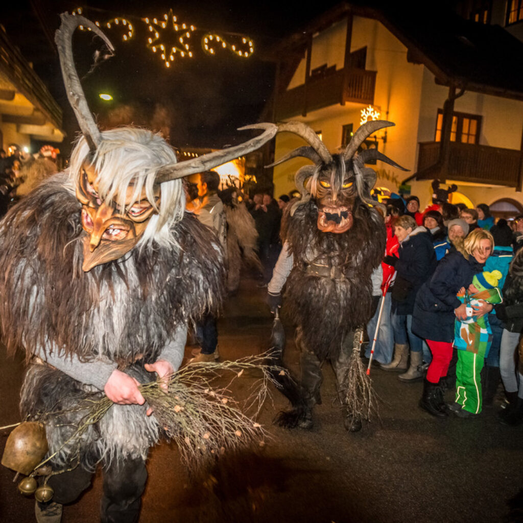 Zwei Menschen in traditionellen österreichischen Krampus-Masken und Pelzkostümen gehen nachts durch eine Menschenmenge.