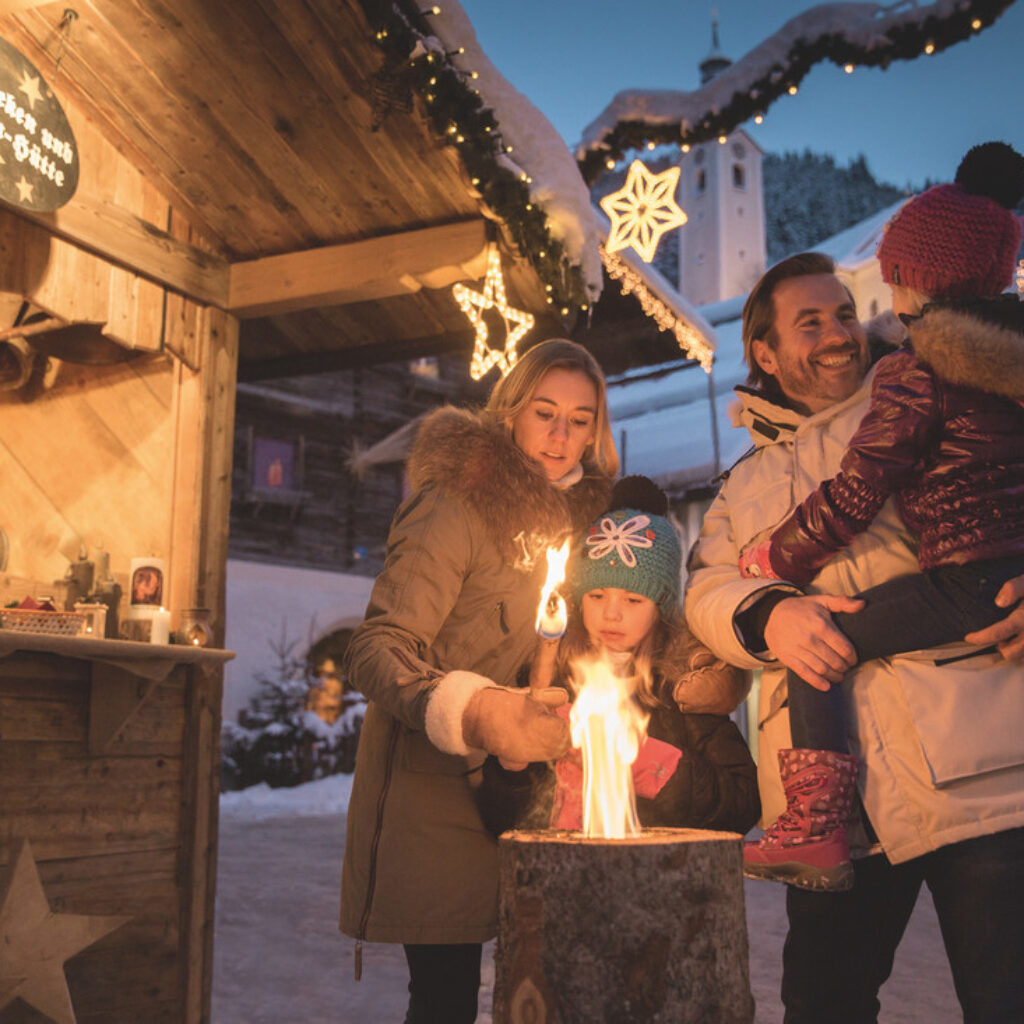 Eine Familie wärmt sich an einem Holzfeuer auf einem österreichischen Weihnachtsmarkt die Hände.