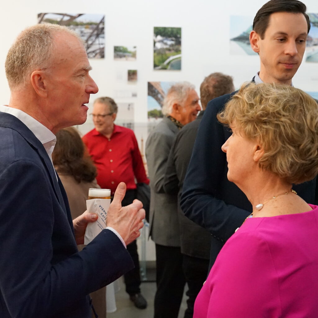 Eine Gruppe von Menschen, die sich bei einer Veranstaltung in einem Gebäude treffen, mit zwei Personen im Vordergrund, die sich unterhalten.