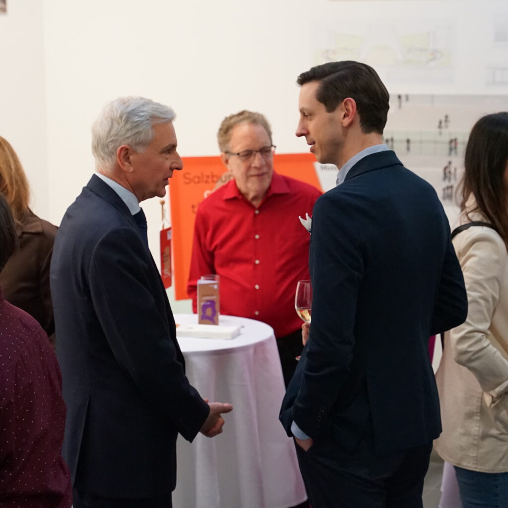 Menschen, die sich bei einer Kunst- oder Architekturausstellung unterhalten und sich unter die Besucher mischen, die an den Wänden hinter ihnen ausgestellt sind.