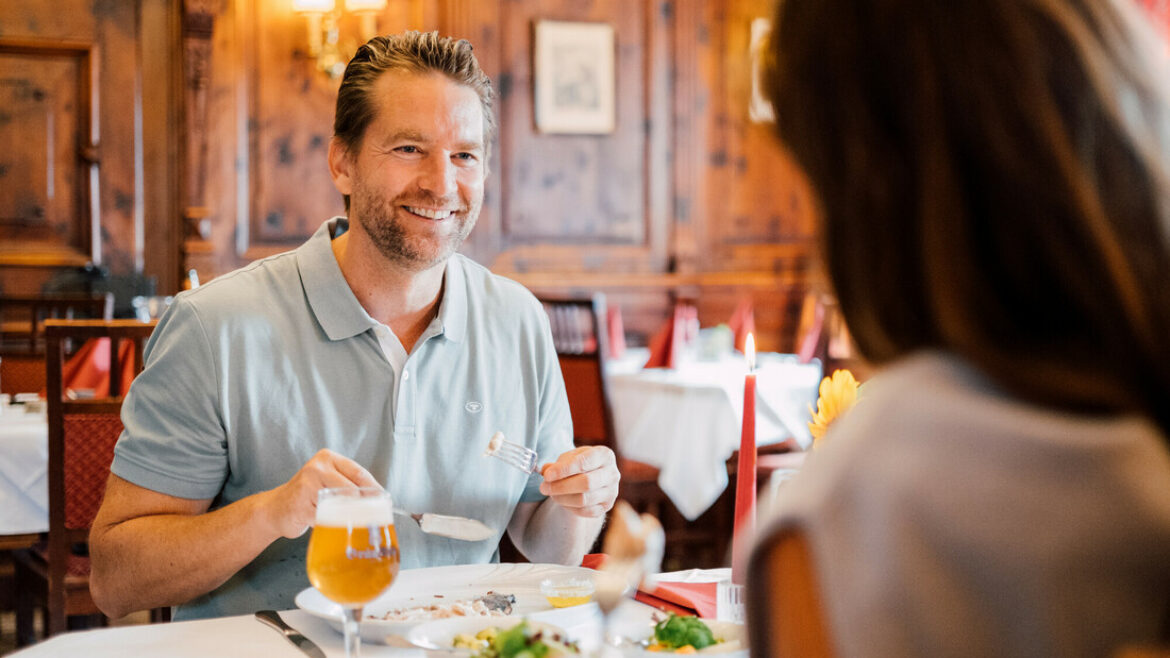Ein lächelnder Mann genießt eine Mahlzeit mit einer Frau in einem warm beleuchteten, eleganten Speisesaal eines Restaurants.