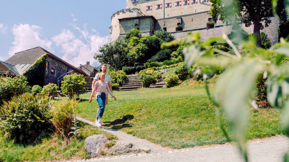 Ein Paar geht an einem sonnigen Tag einen Gartenweg hinauf in Richtung eines großen historischen Gebäudes.