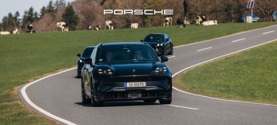Drei schwarze Porsche fahren auf einer kurvenreichen Landstraße, im Hintergrund sind Gras und Kühe zu sehen.