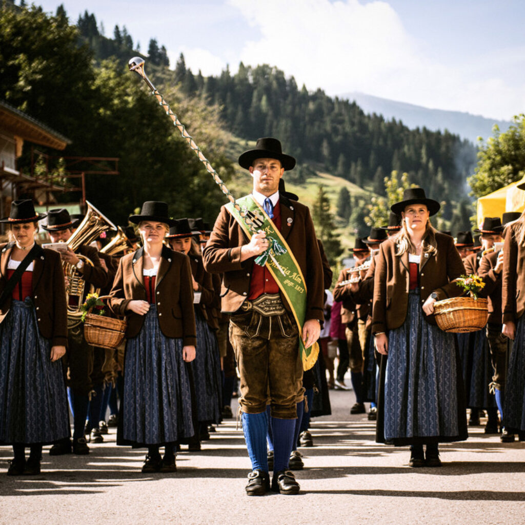 Menschen in traditioneller österreichischer Tracht ziehen in einem Umzug vorbei und tragen Körbe und Musikinstrumente.