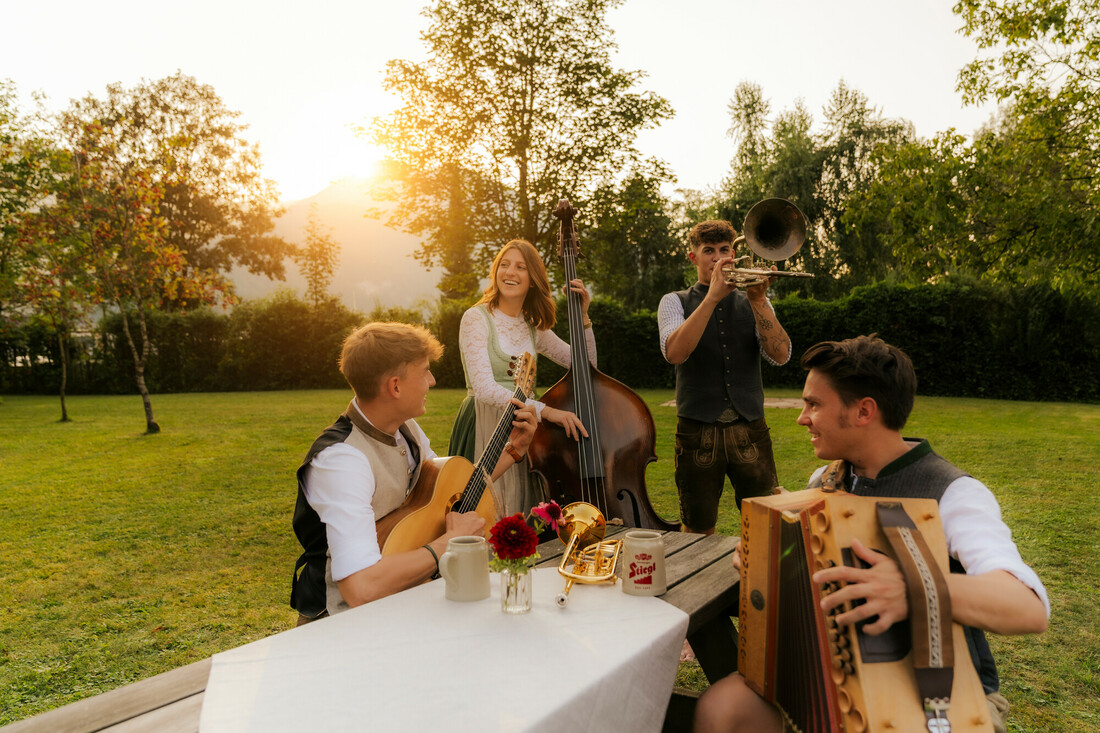 Vier Menschen in traditioneller Tracht spielen im Freien auf Instrumenten – echte kulturelle Sommer-Highlights bei Sonnenuntergang.