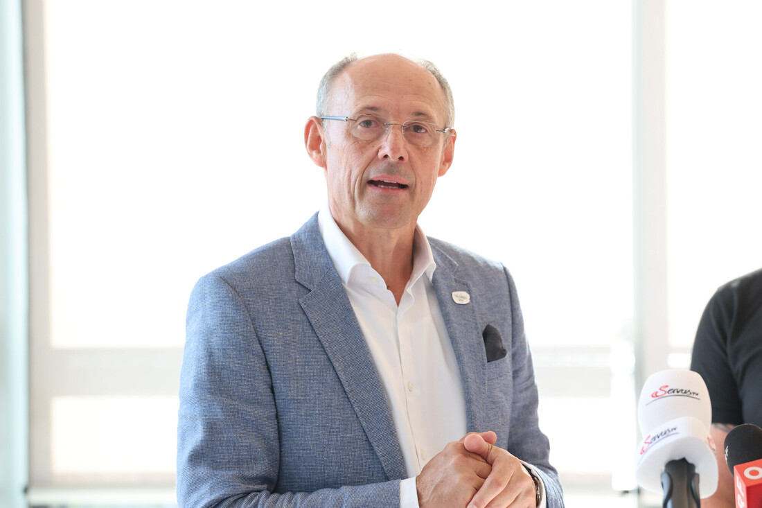 Ein Mann mittleren Alters in einem blauen Blazer, der in Mikrofone spricht.